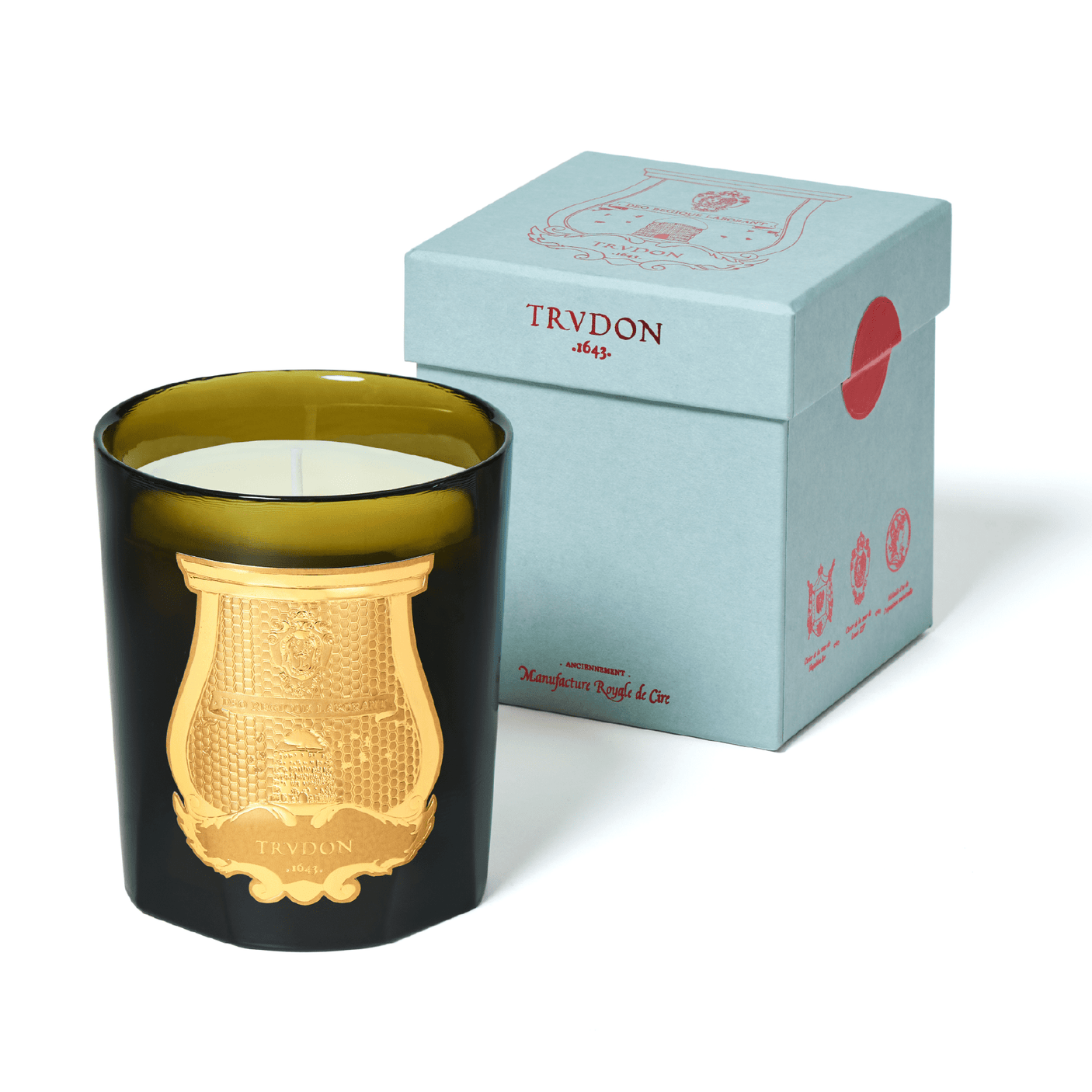 A candle in a green glass container with a golden logo, presented in luxurious blue packaging