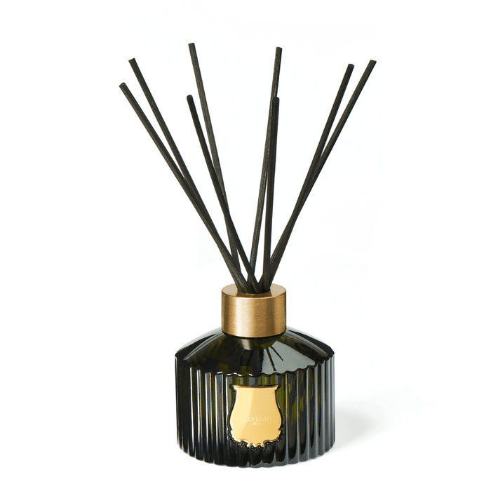 A diffuser in a green glass container adorned with a golden emblem